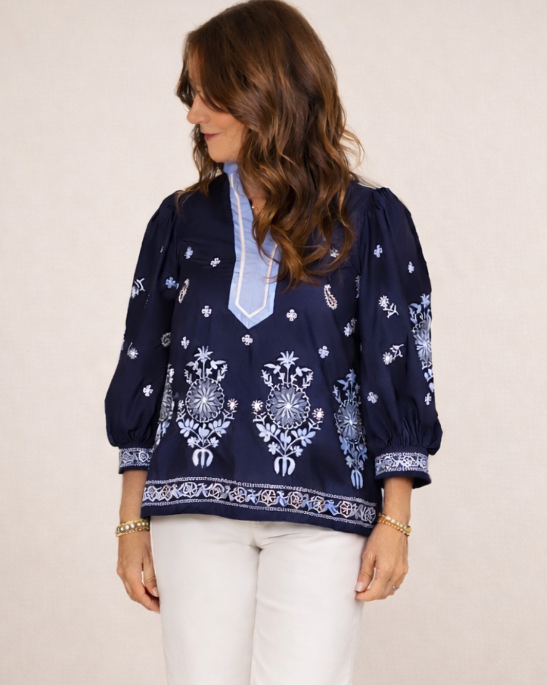 Woman wearing a navy blouse with white embroidery on a plain background