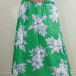 Woman wearing a green dress with floral pattern against a plain background