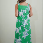 Person wearing a green floral dress standing against a plain wall.