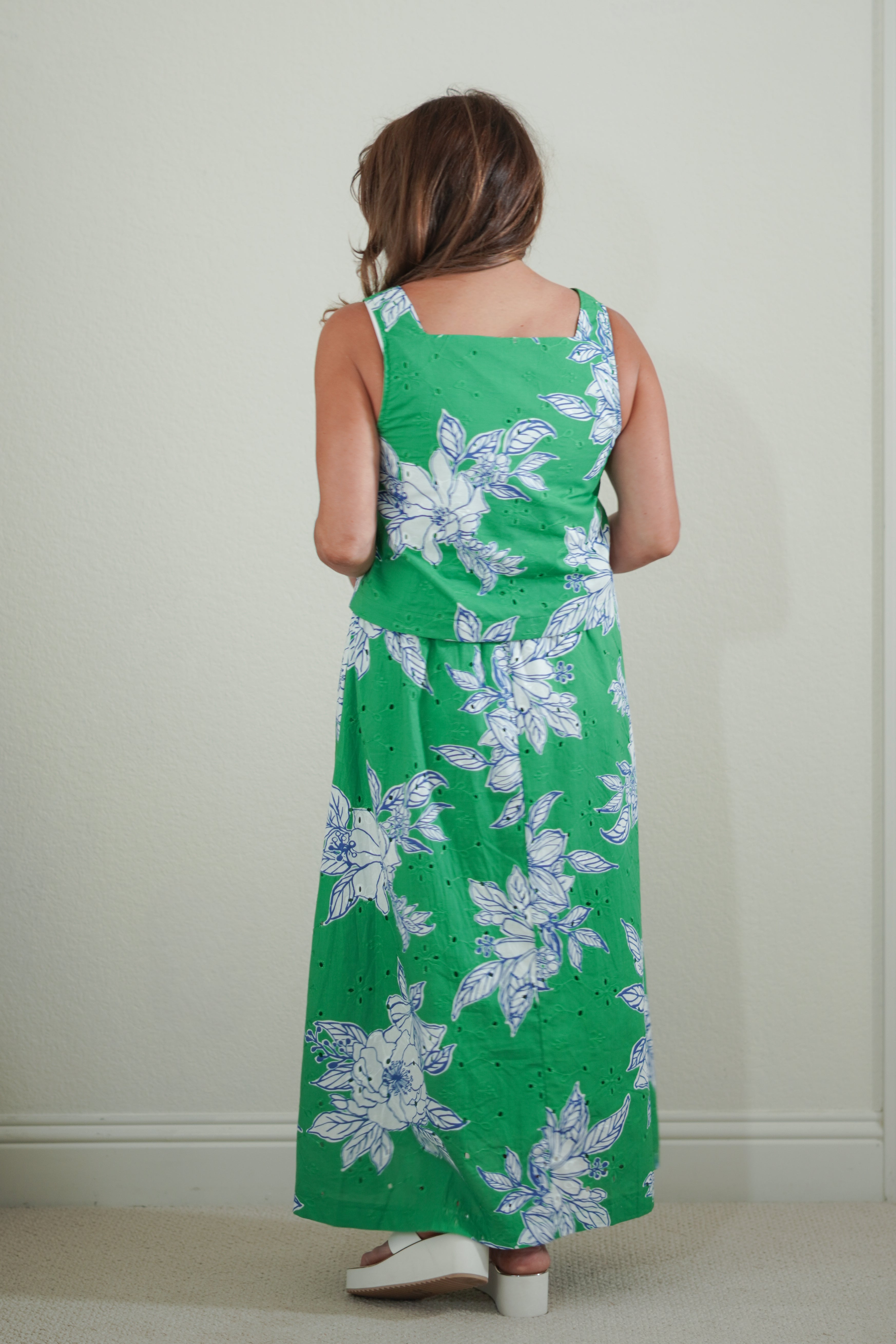 Person wearing a green floral dress standing against a plain wall.