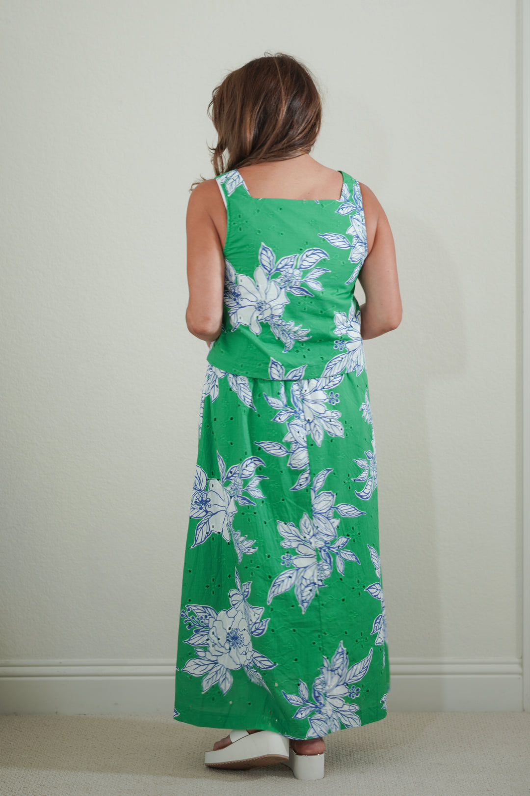 Person wearing a green floral dress standing against a plain wall.