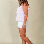 Woman wearing a light pink sleeveless top and white shorts against a beige background