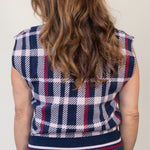 A woman viewed from behind wearing a navy, white, and red plaid sleeveless top with a striped hem, paired with blue jeans.