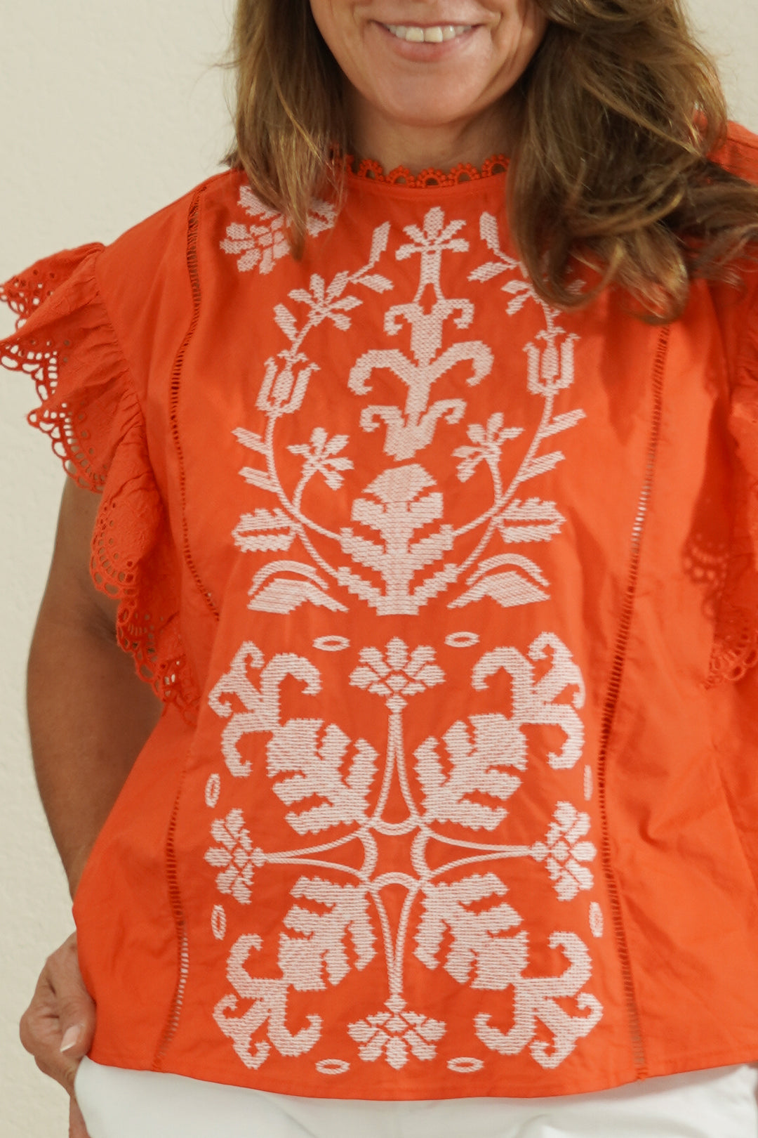 Person wearing an orange top with white floral embroidery against a plain background