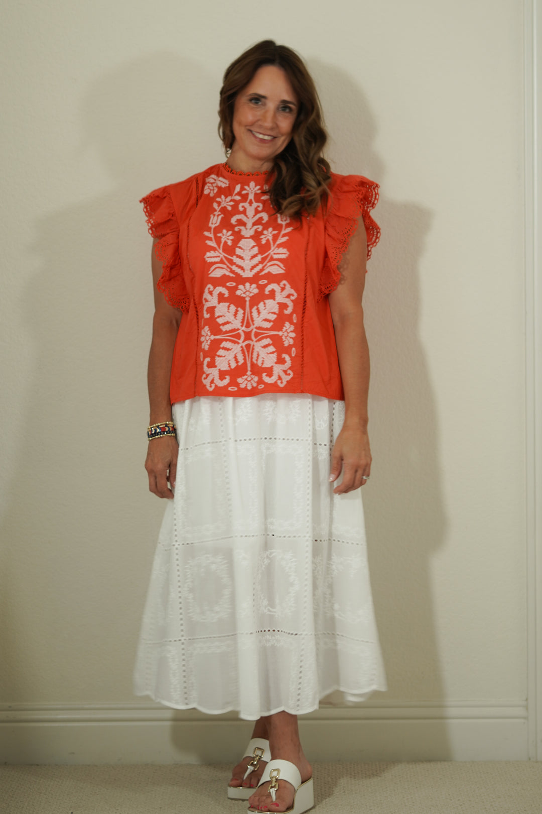 Woman wearing a red top with white floral patterns and a white skirt against a plain background