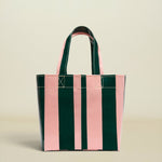 A glossy vertical-striped tote bag with alternating dark green and light pink panels, featuring dark green handles with pink lining, set against a solid light beige background.