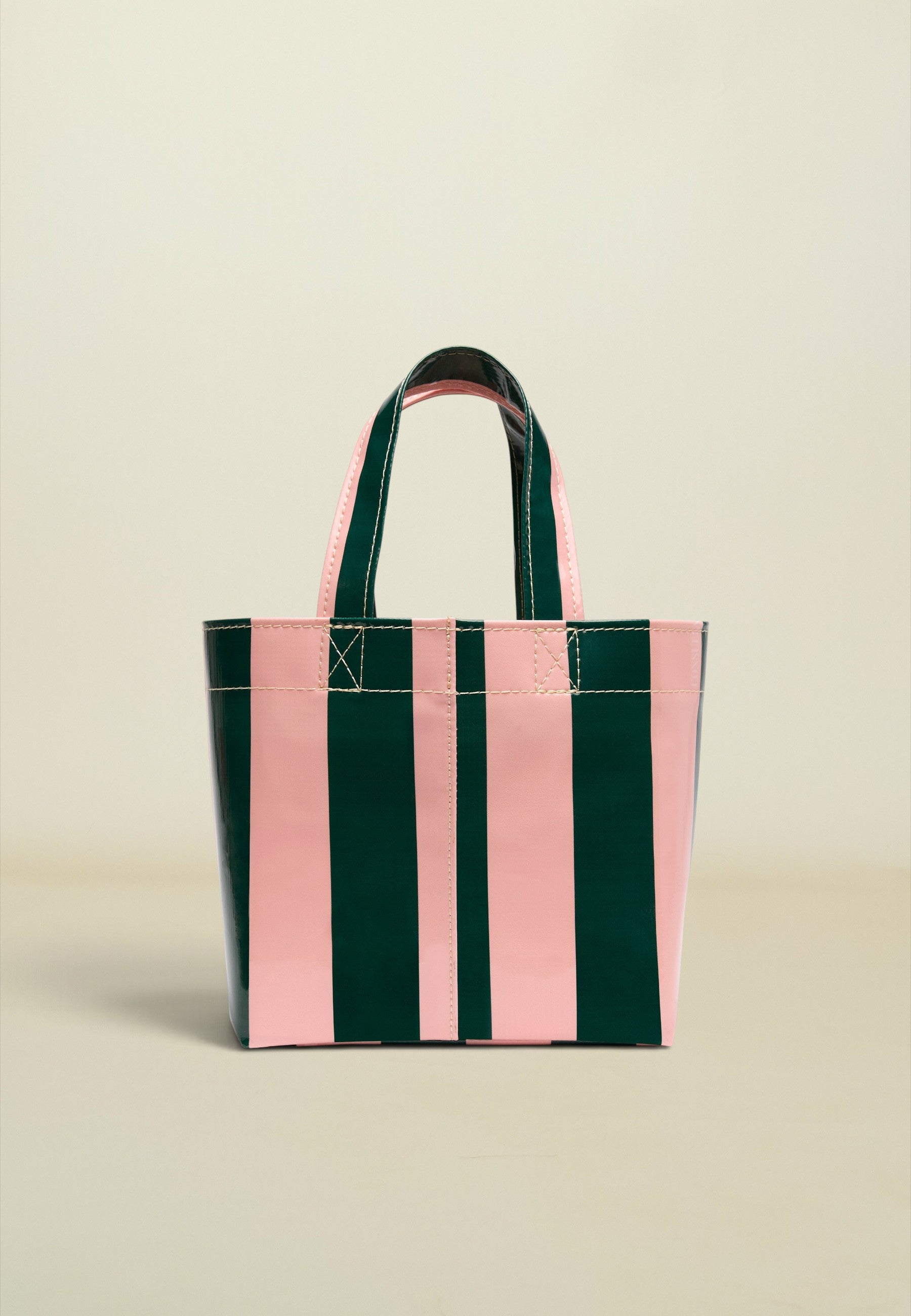 A glossy vertical-striped tote bag with alternating dark green and light pink panels, featuring dark green handles with pink lining, set against a solid light beige background.