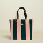 A structured tote bag with vertical pink and dark green stripes, featuring dual top handles and a small gold-tone metal plaque on the front, set against a solid light beige background.