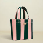 A striped tote bag with alternating vertical pink and dark green stripes, featuring dark green handles and a small gold-tone metal plaque on the front.