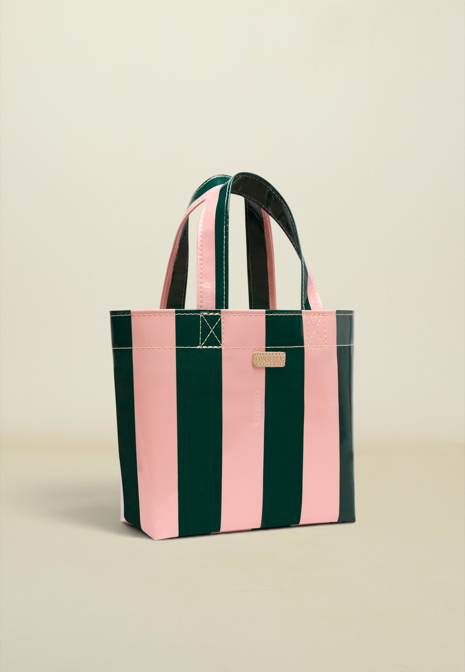 A striped tote bag with alternating vertical pink and dark green stripes, featuring dark green handles and a small gold-tone metal plaque on the front.