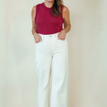 A woman modeling a sleeveless magenta top and white wide-leg pants against a plain beige studio background.
