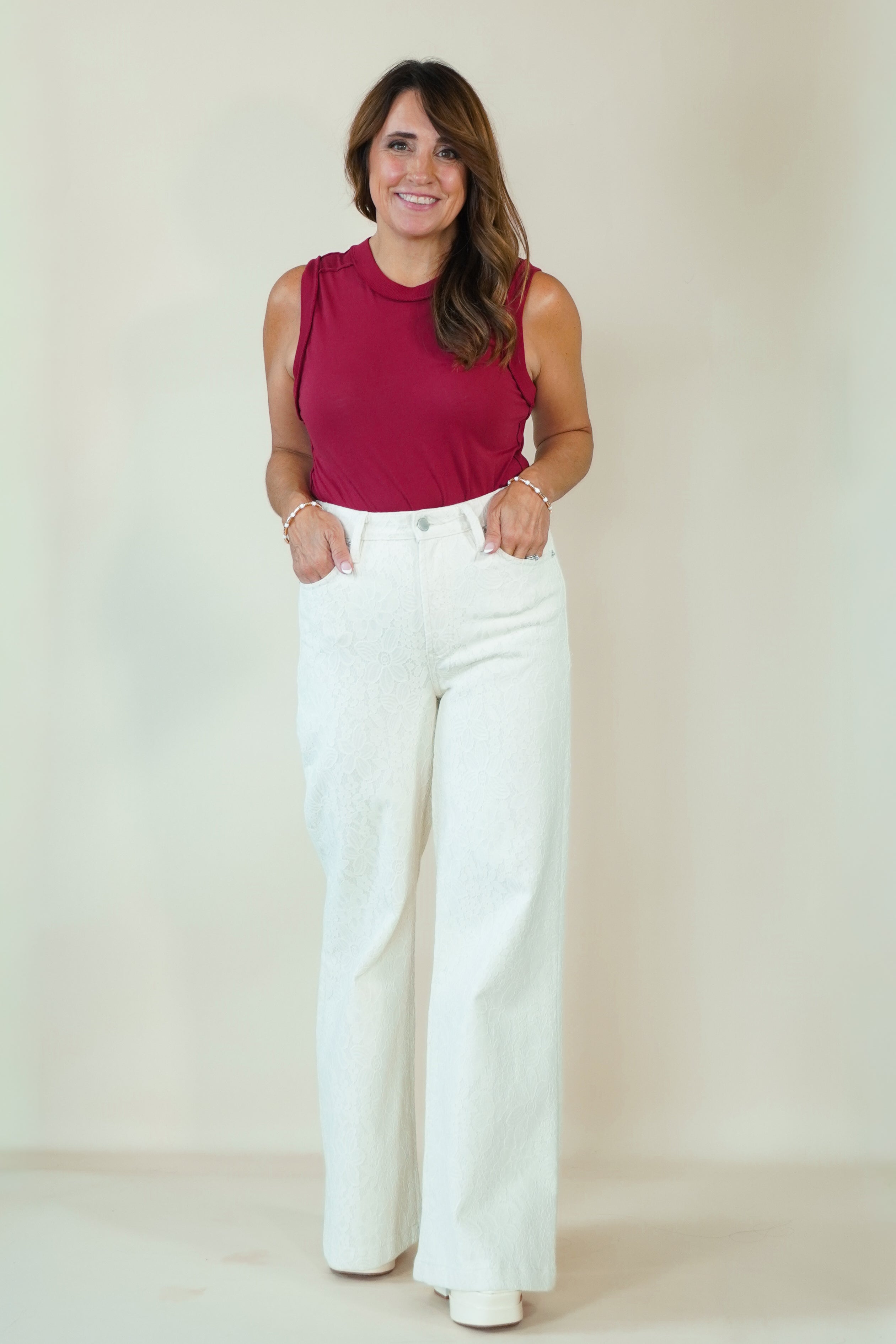 A woman modeling a sleeveless magenta top and white wide-leg pants against a plain beige studio background.