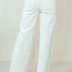 White wide-leg pants shown from the back on a model, paired with a dark red top and white heels, against a plain beige studio background.