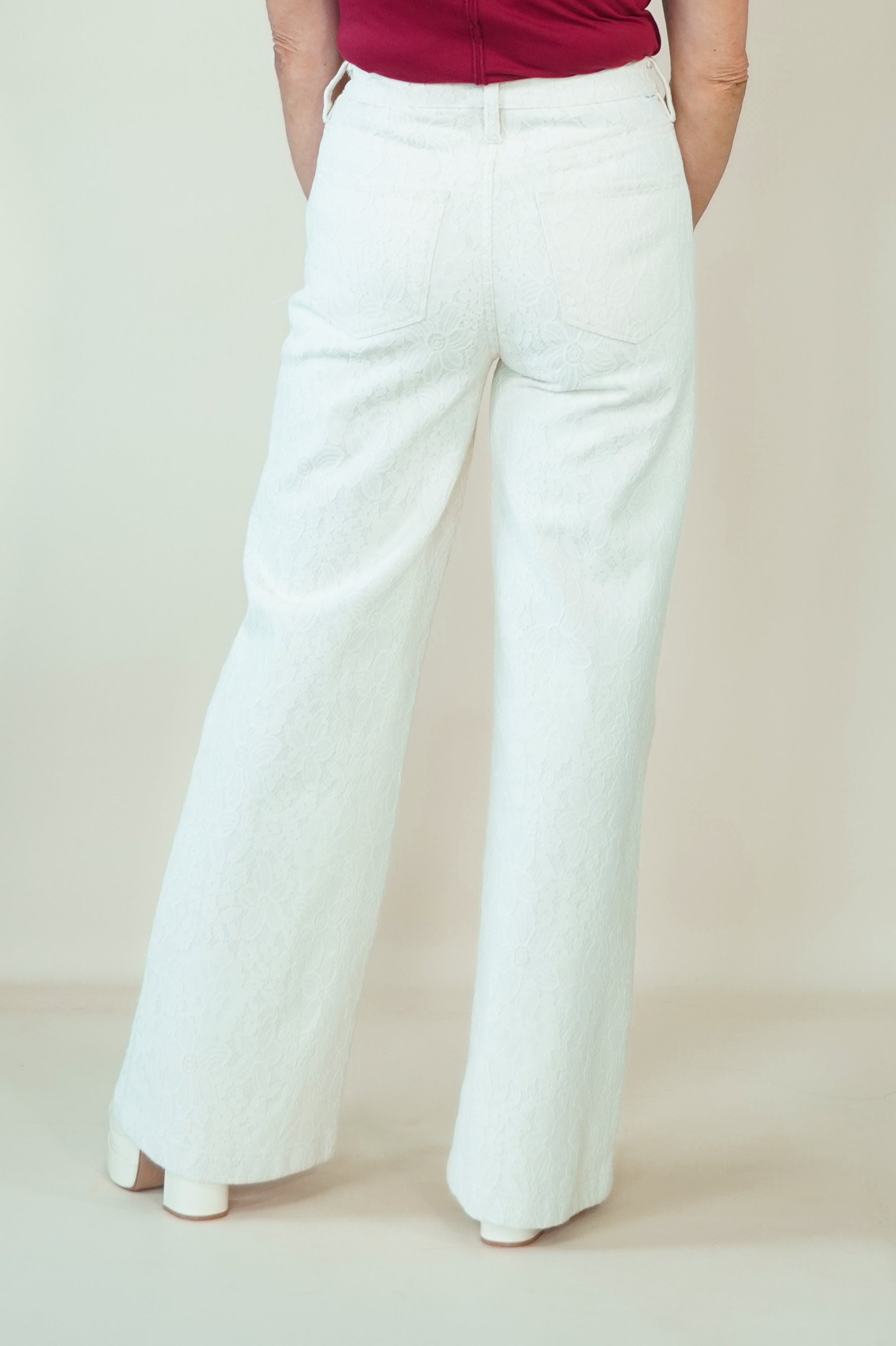 White wide-leg pants shown from the back on a model, paired with a dark red top and white heels, against a plain beige studio background.