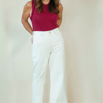 A woman modeling a sleeveless magenta top and white wide-leg pants against a plain beige studio backdrop.