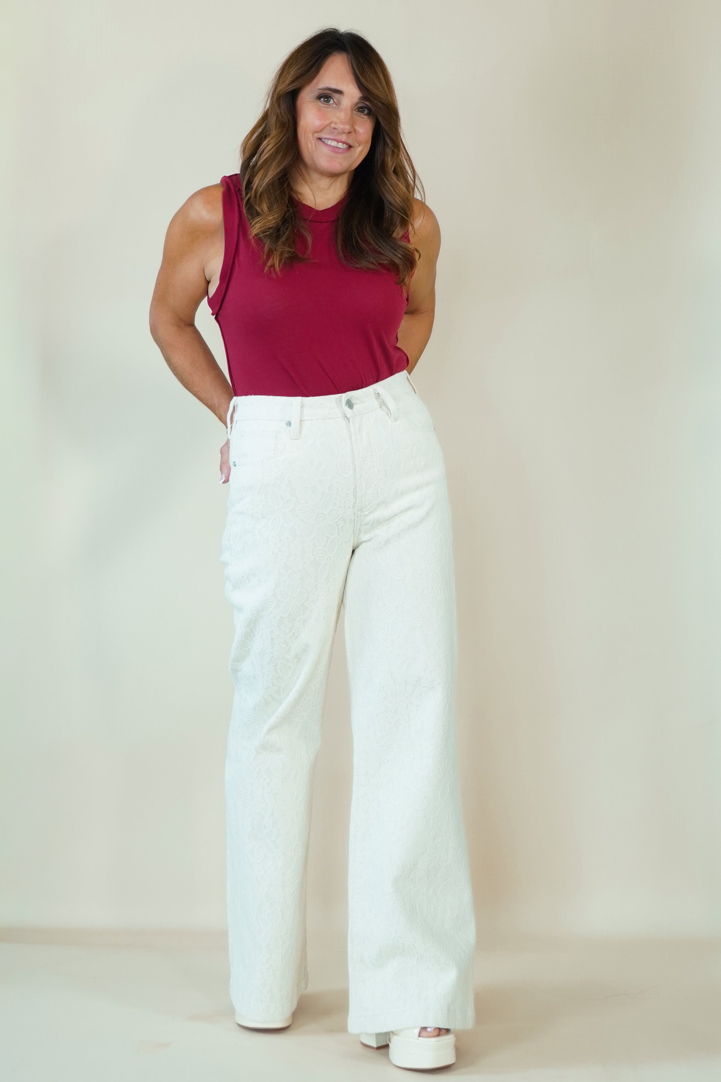 A woman modeling a sleeveless magenta top and white wide-leg pants against a plain beige studio backdrop.