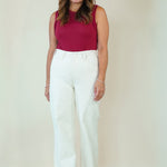 A woman modeling a sleeveless burgundy top and high-waisted white wide-leg pants against a plain beige studio background.