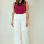 A woman modeling a sleeveless burgundy top and white wide-leg pants against a plain beige studio background.