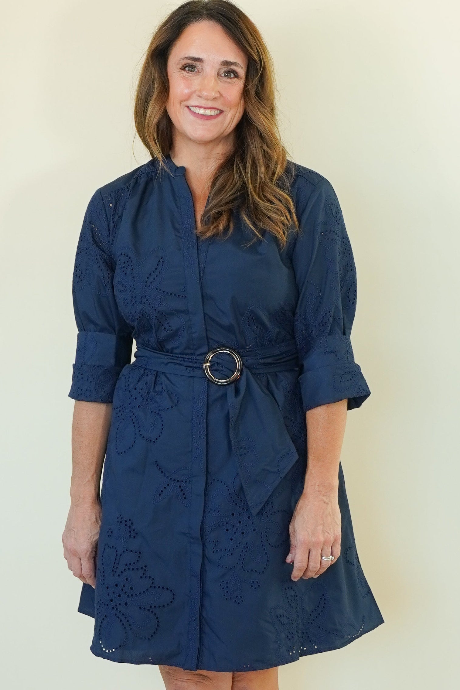 A woman modeling a navy blue midi dress with a matching belt and a subtle tonal floral jacquard pattern, standing against a plain cream-colored background.