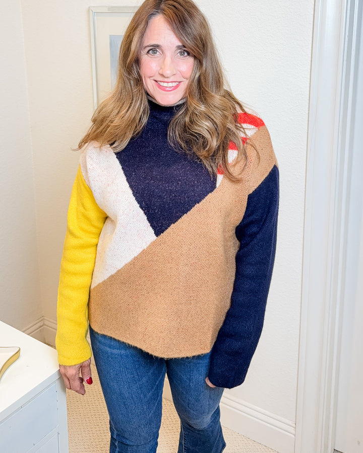 Woman wearing a colorful sweater in a room with a lamp and framed picture on the wall.
