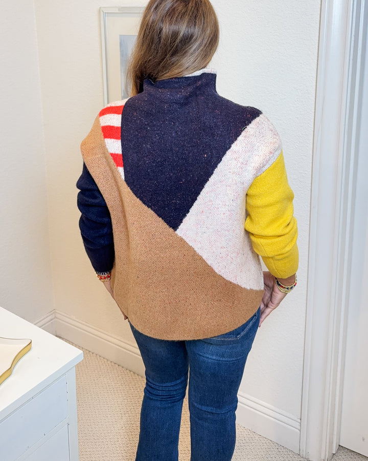 Person wearing a colorful sweater standing in a room with framed artwork on the wall.