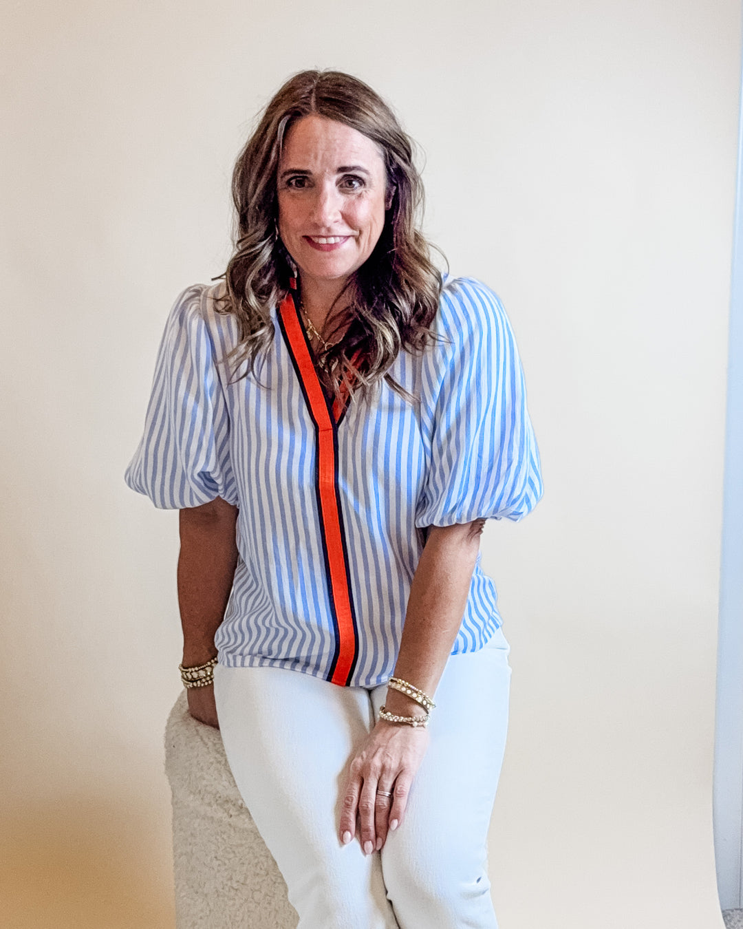 Woman wearing a blue and white striped blouse with a red zipper, sitting against a plain background.