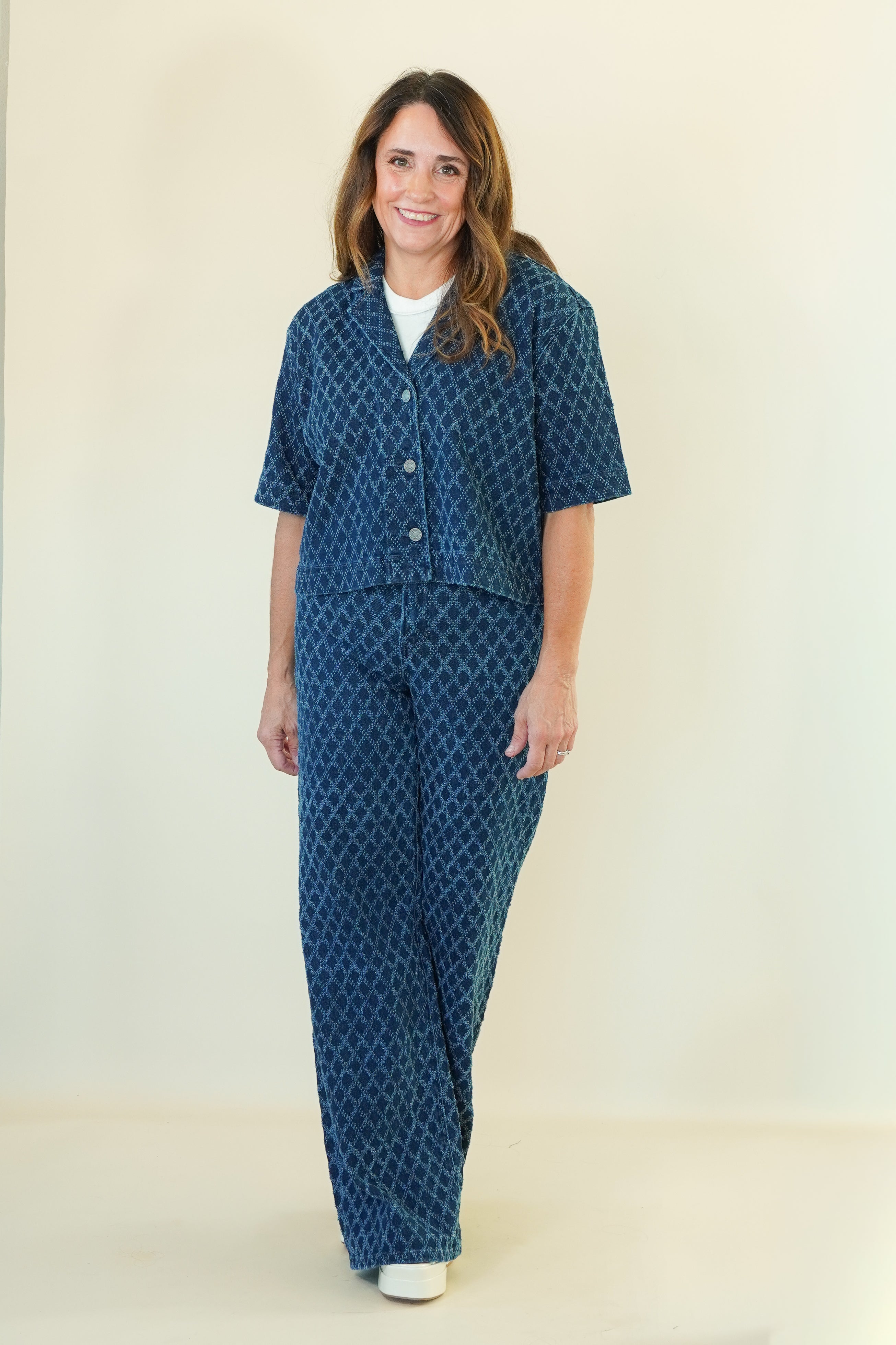 A woman modeling a matching two-piece lounge set featuring a short-sleeve button-front top and wide-leg pants, both in a dark blue with a lighter blue geometric pattern, over a white undershirt.