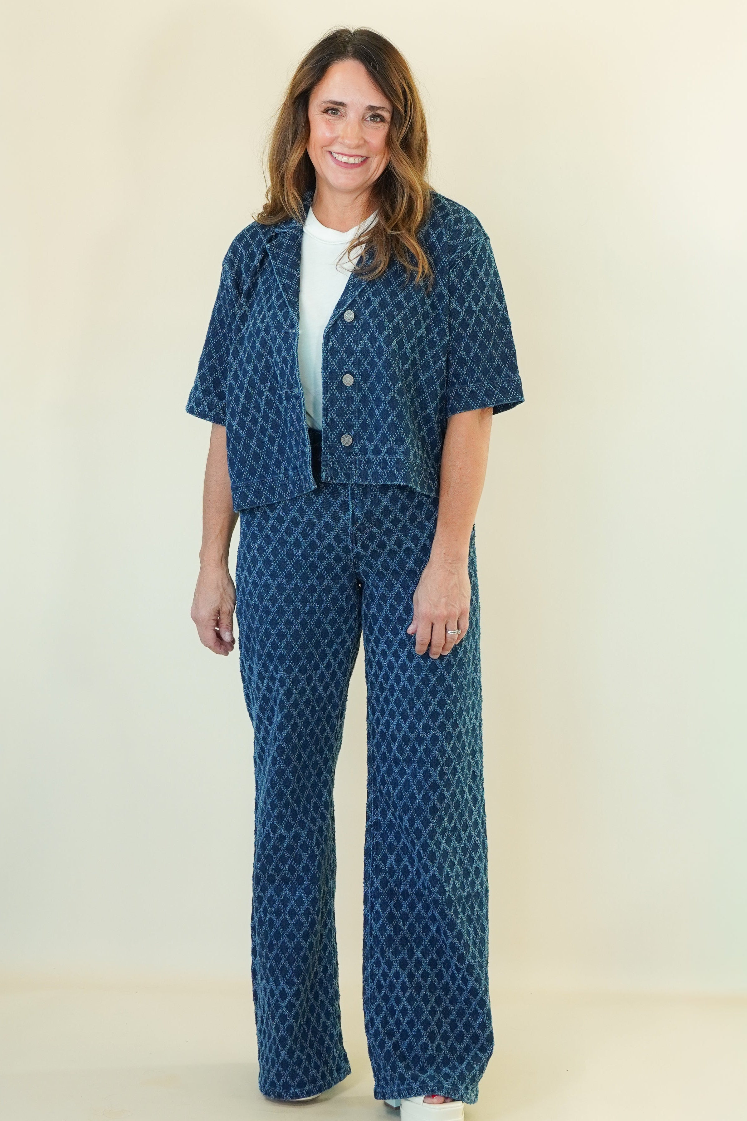 A woman modeling a matching two-piece outfit consisting of a short-sleeve button-front jacket and wide-leg pants, both in a blue and white geometric pattern, against a plain cream background.
