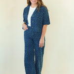 A woman modeling a matching two-piece lounge set featuring a short-sleeve button-front cardigan and wide-leg pants in a blue and white geometric pattern, styled over a white t-shirt.