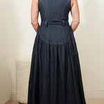 back view of a person wearing a long denim dress with a belt against a neutral background