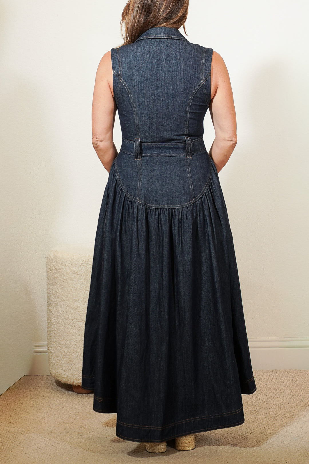 back view of a person wearing a long denim dress with a belt against a neutral background