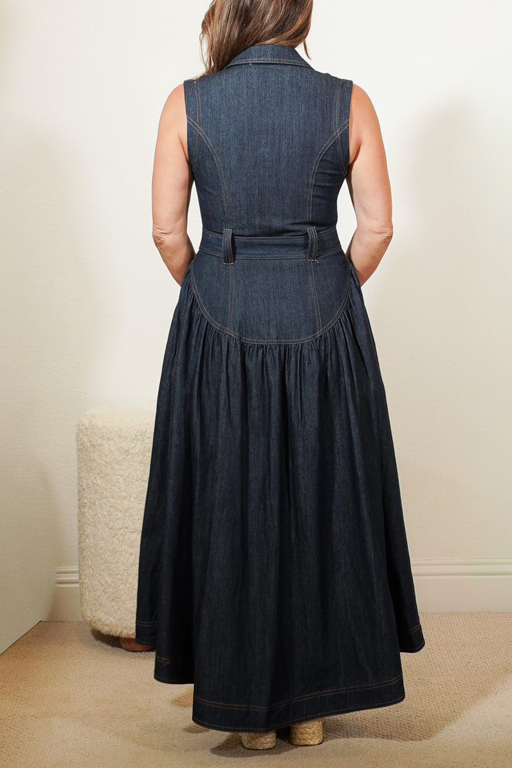 back view of a person wearing a long denim dress with a belt against a neutral background