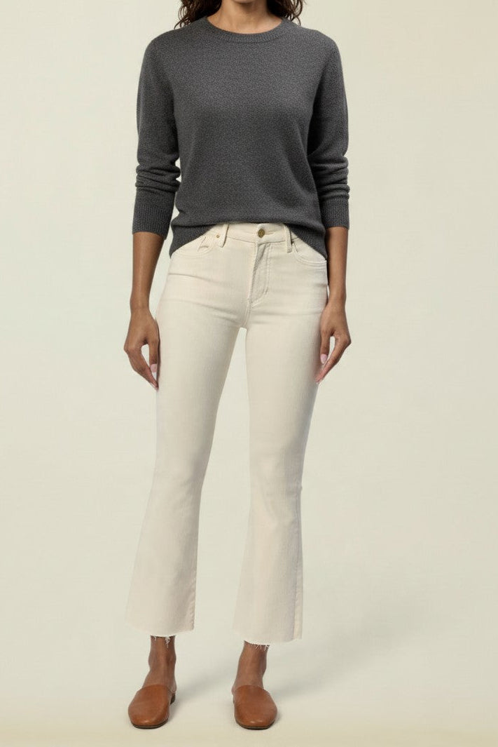 A woman modeling a dark gray long-sleeve knit sweater and off-white cropped jeans with brown flat shoes, standing against a solid light beige studio background.