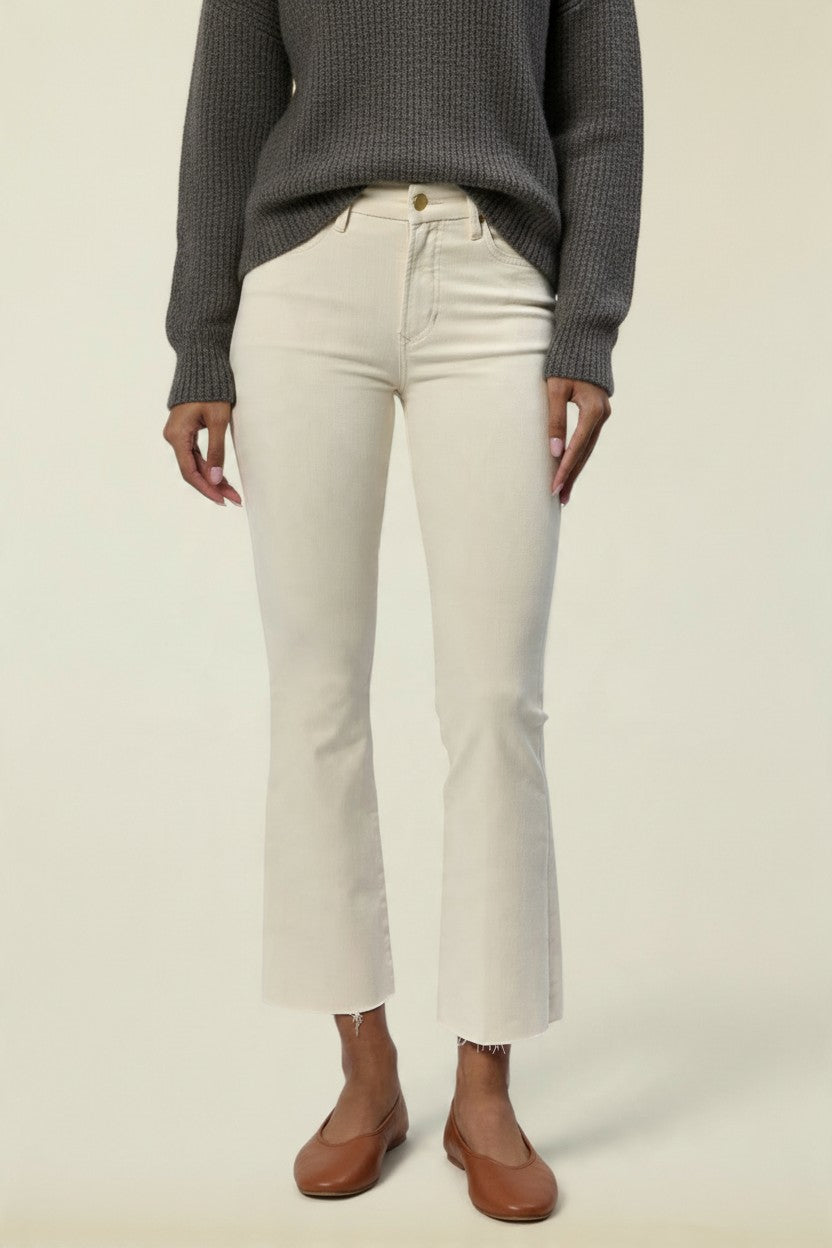 A model wearing off-white cropped flare jeans, a dark gray ribbed knit sweater, and brown leather flats, shown from the chest down against a plain light beige studio background.