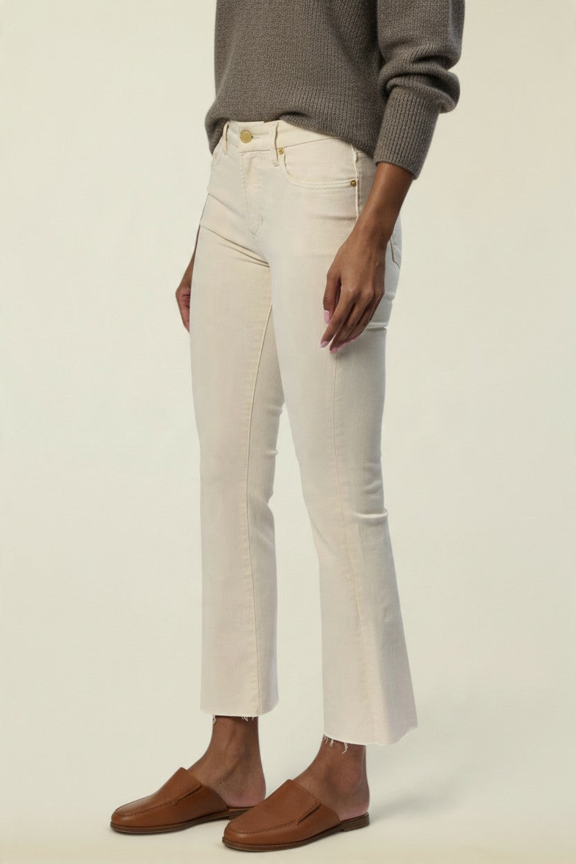 A model wearing off-white cropped jeans with a side seam detail, styled with a gray knit sweater and brown leather loafers against a plain cream background.