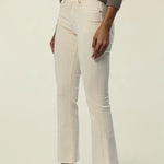 A model wearing off-white cropped jeans with a side seam detail, styled with a gray knit sweater and brown leather loafers against a plain cream background.