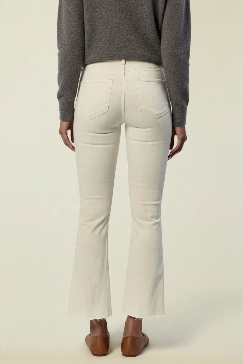A person shown from the back wearing off-white flared jeans, a dark gray long-sleeve top, and brown flat shoes against a plain light beige studio background.