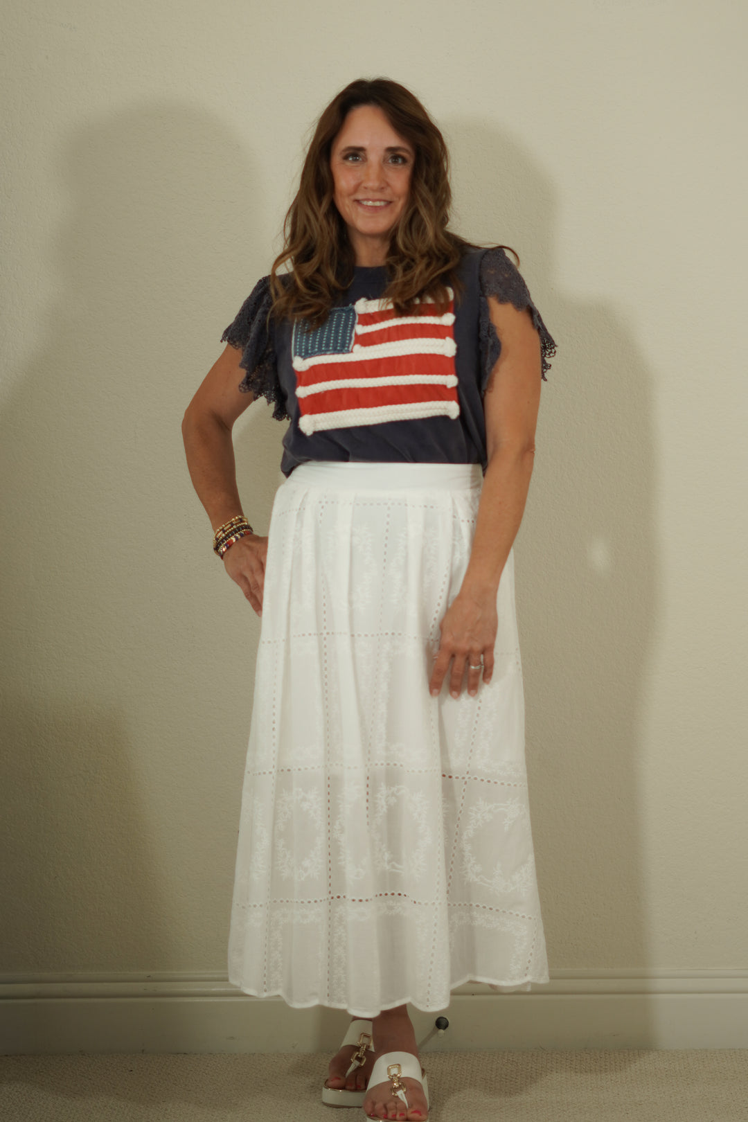 Woman wearing a colorful top with an American flag design and a white skirt against a plain background