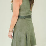 A woman wearing a sleeveless olive green dress with a matching belt and wedge sandals, photographed from the back against a plain light background.