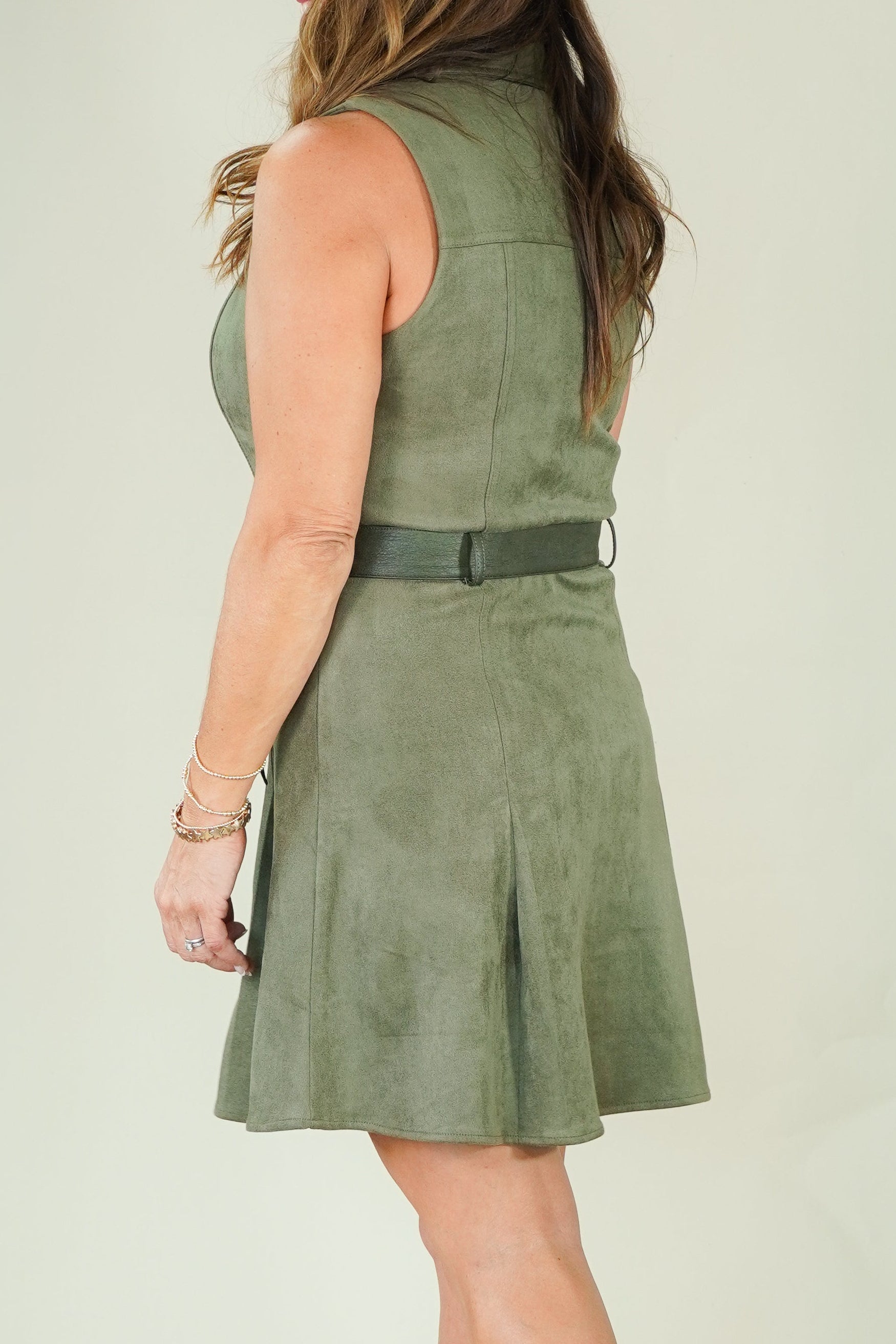 A woman wearing a sleeveless olive green dress with a matching belt and wedge sandals, photographed from the back against a plain light background.