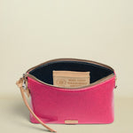 Pink clutch bag with beige strap and visible brand logo on a white background