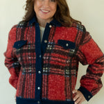 A woman modeling a red and navy plaid button-up jacket with blue jeans and tan ankle boots, standing against a plain white studio background.