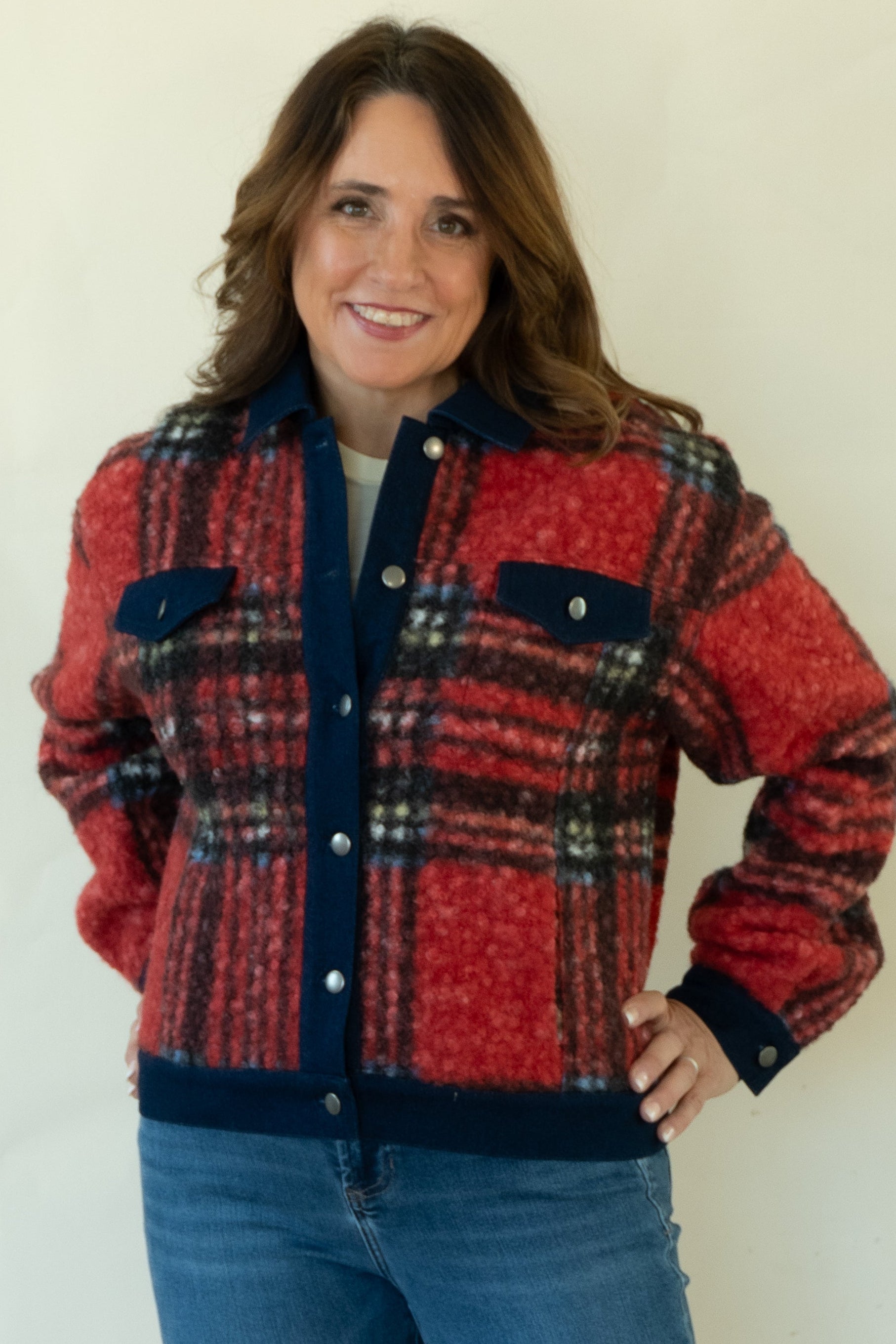 A woman modeling a red and navy plaid button-up jacket with blue jeans and tan ankle boots, standing against a plain white studio background.