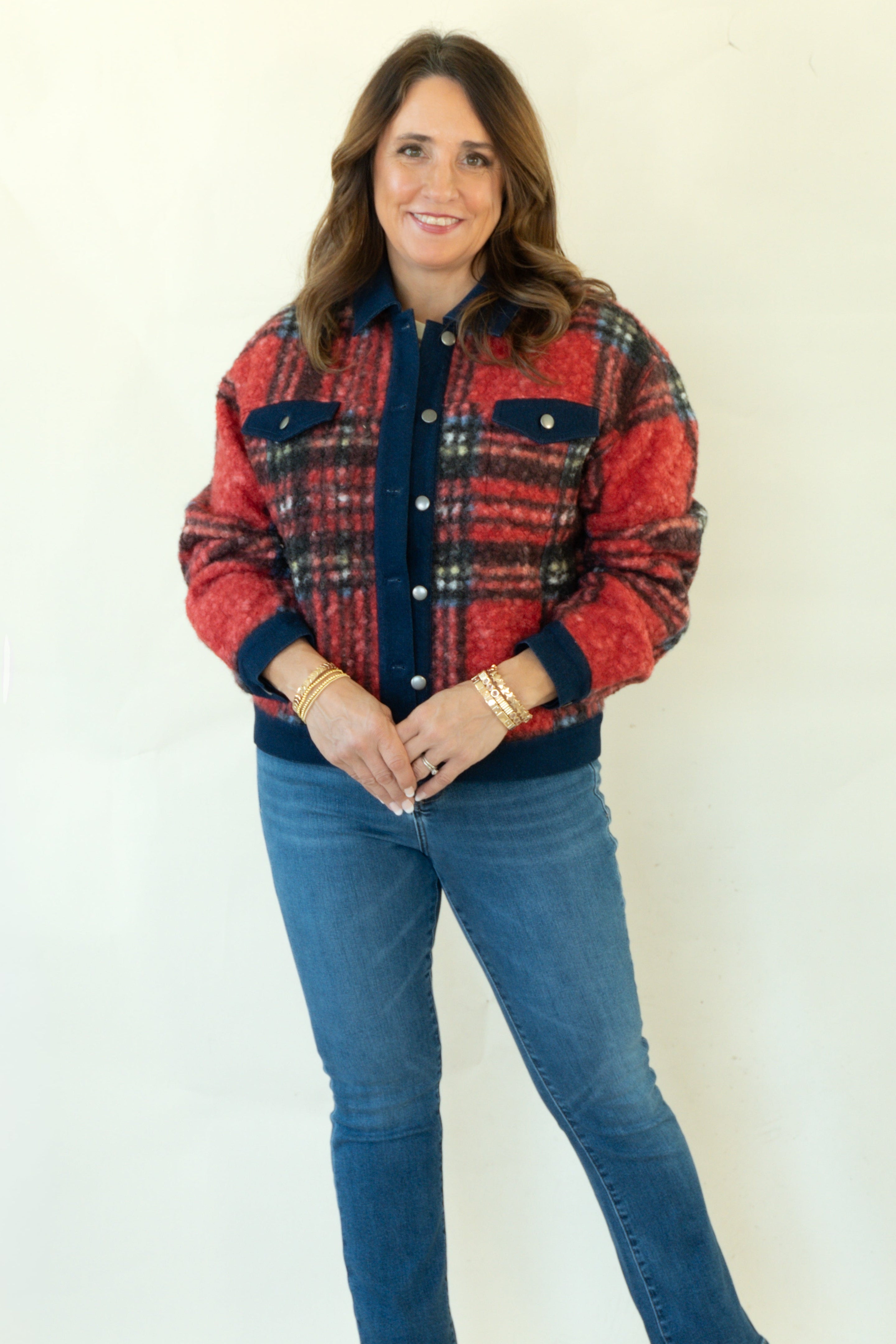 A woman modeling a red and navy plaid button-up jacket with blue jeans and tan ankle boots, standing against a plain white studio background.