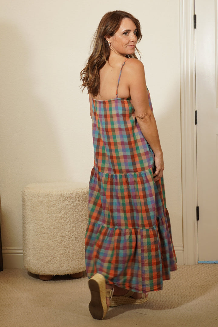 Woman in a plaid dress standing in front of a mirror in a room with white cabinets.