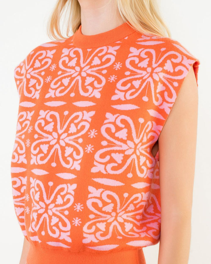 Person wearing an orange sleeveless top with white butterfly pattern on a plain background
