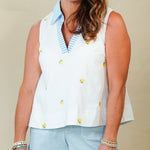 Woman wearing a sleeveless white top with yellow buttons and light blue shorts against a beige background