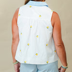 Woman wearing a sleeveless white top with yellow buttons and light blue shorts on a beige background