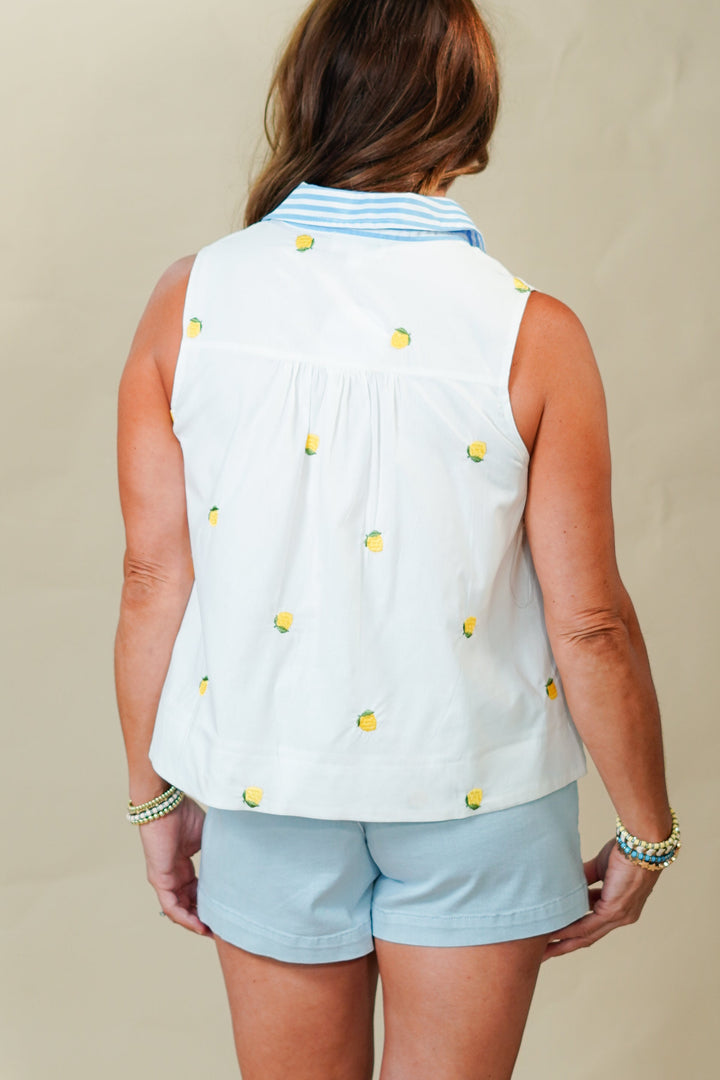 Woman wearing a sleeveless white top with yellow buttons and light blue shorts on a beige background