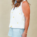 Woman wearing a white sleeveless top with yellow buttons and light blue shorts on a beige background